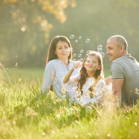 Happy Family With Child Girl Blow Soap Bubbles Outdoor In Sunny