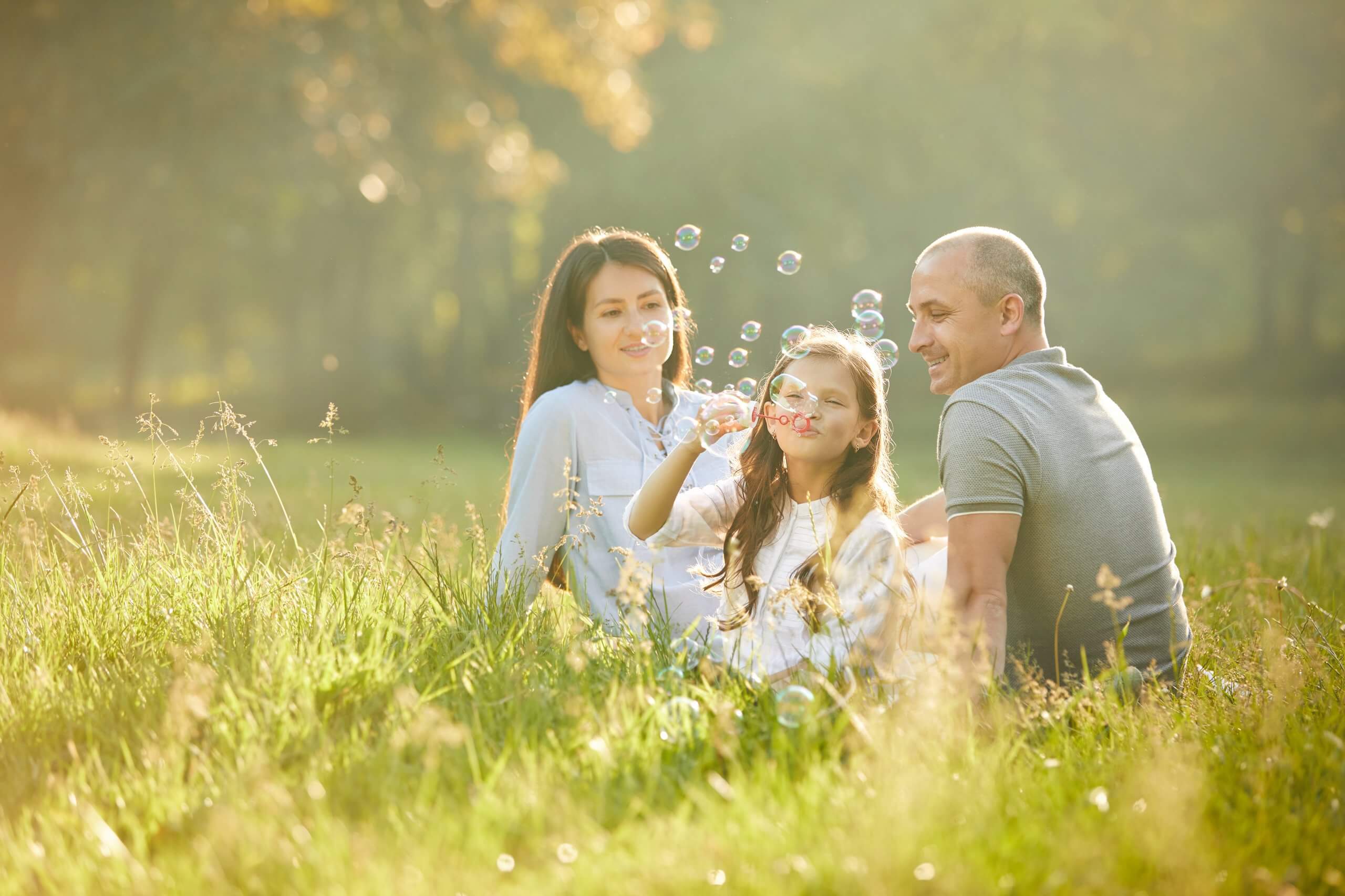 Happy Family With Child Girl Blow Soap Bubbles Outdoor In Sunny