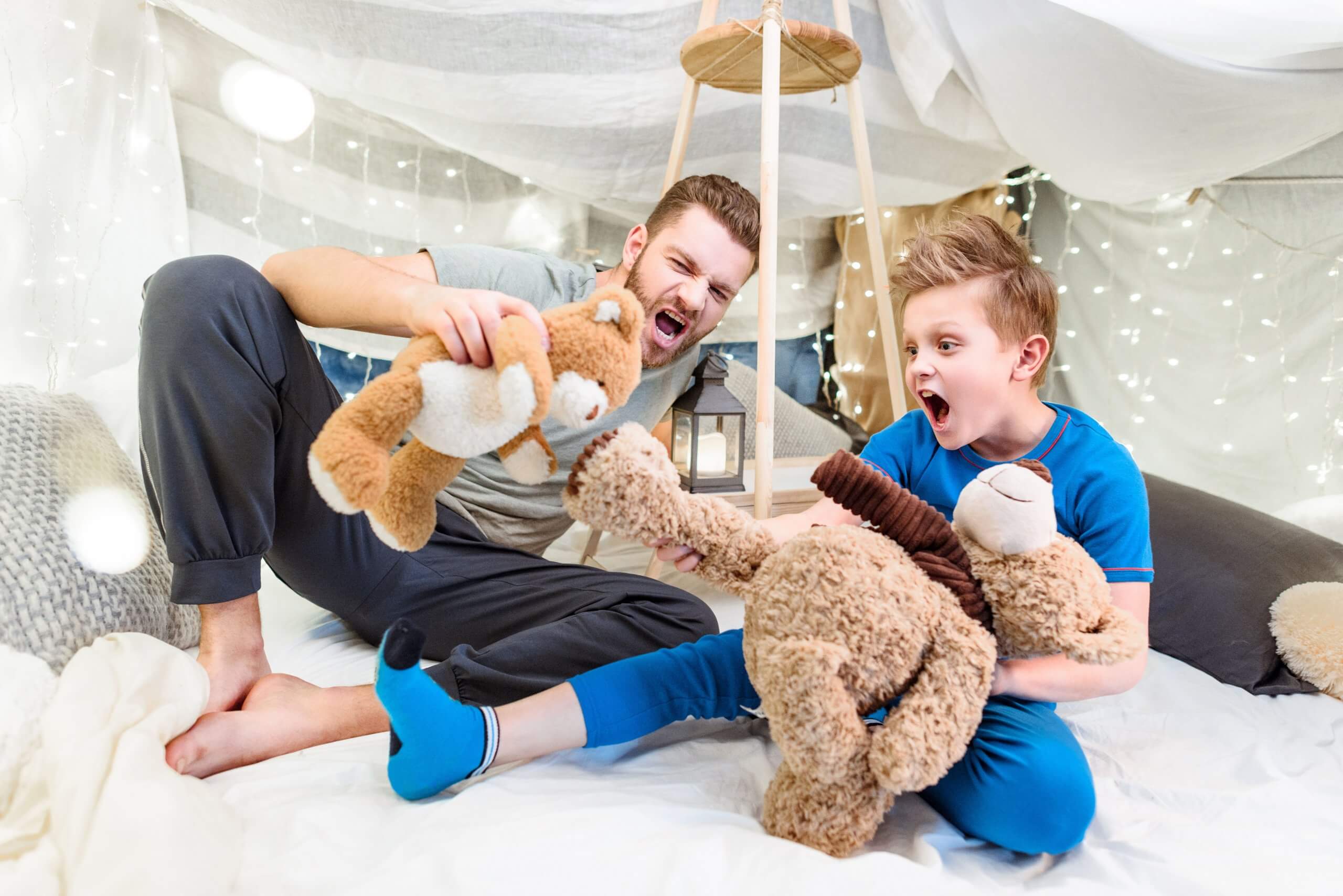 Excited Father And Son Sitting In Blanket Fort And Playing With